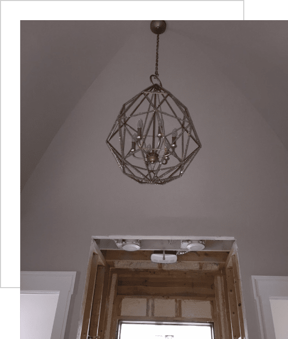 Geometric metal chandelier hanging from a high, arched ceiling above a partially constructed doorway.